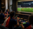Des amis regardent un match de football à la télévision et sur des appareils mobiles dans un salon